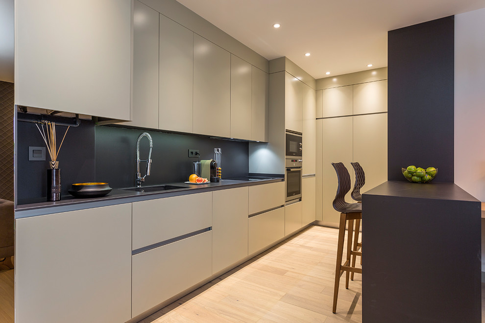 Photo of a mid-sized contemporary l-shaped open plan kitchen in Madrid with an integrated sink, flat-panel cabinets, beige cabinets, quartz benchtops, black splashback, stainless steel appliances, light hardwood floors and beige floor.