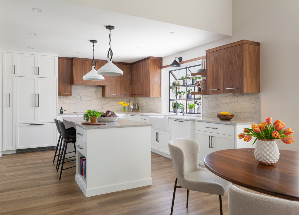 Inspiration for a mid-sized transitional l-shaped eat-in kitchen in Minneapolis with a farmhouse sink, flat-panel cabinets, white cabinets, quartzite benchtops, grey splashback, stone slab splashback, panelled appliances, vinyl floors, with island, brown floor and grey benchtop.