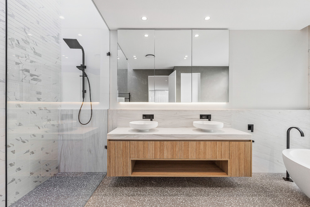 Mid-sized contemporary master bathroom in Melbourne with flat-panel cabinets, light wood cabinets, a freestanding tub, an alcove shower, white walls, a vessel sink, white benchtops, a wall-mount toilet, white tile, marble, terrazzo floors, marble benchtops and grey floor.