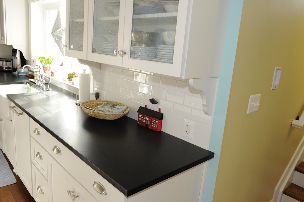 Example of a large transitional u-shaped medium tone wood floor enclosed kitchen design in Baltimore with a farmhouse sink, glass-front cabinets, white cabinets, soapstone countertops, white backsplash, subway tile backsplash, stainless steel appliances and an island