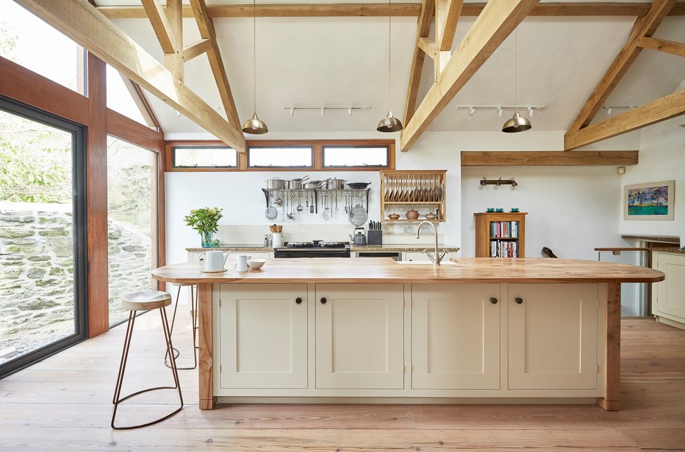 This is an example of a mid-sized country galley open plan kitchen in Devon with a farmhouse sink, shaker cabinets, beige cabinets, wood benchtops, beige splashback, ceramic splashback, stainless steel appliances, medium hardwood floors, with island, brown floor and brown benchtop.