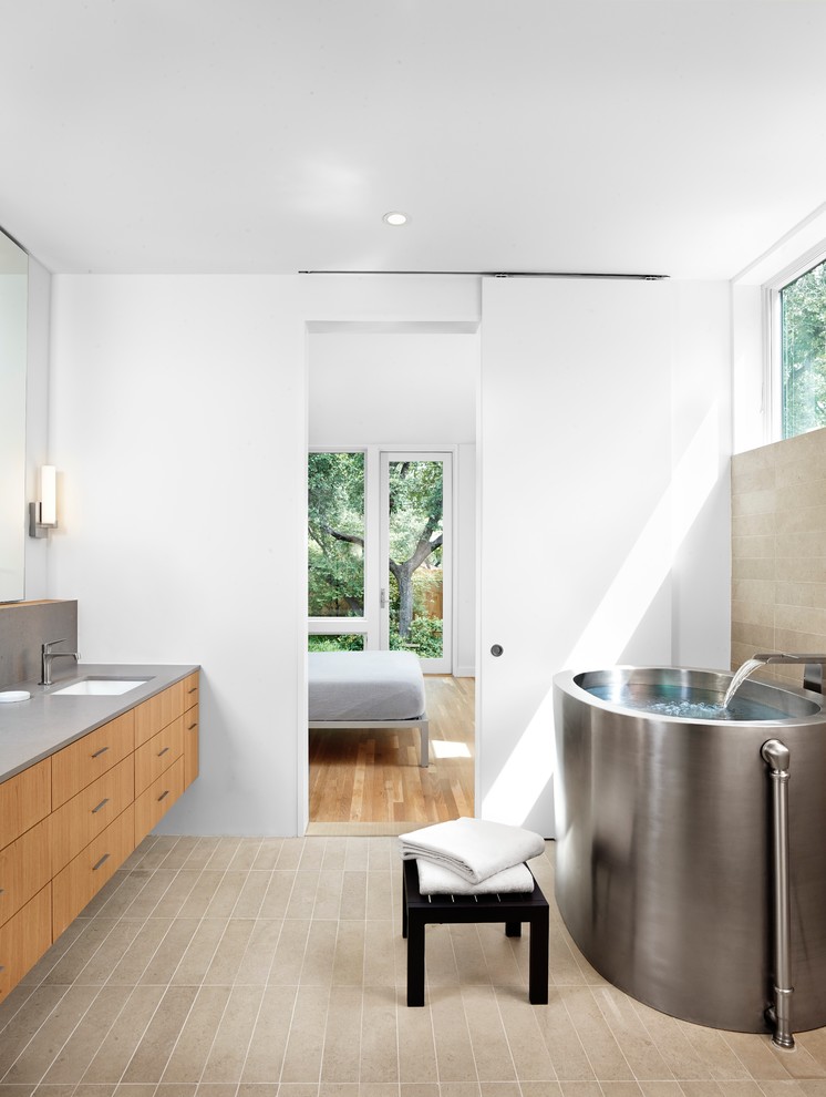 Mid-sized modern master bathroom in Austin with flat-panel cabinets, engineered quartz benchtops, a freestanding tub, stone slab, an undermount sink, white walls, medium wood cabinets and beige tile.