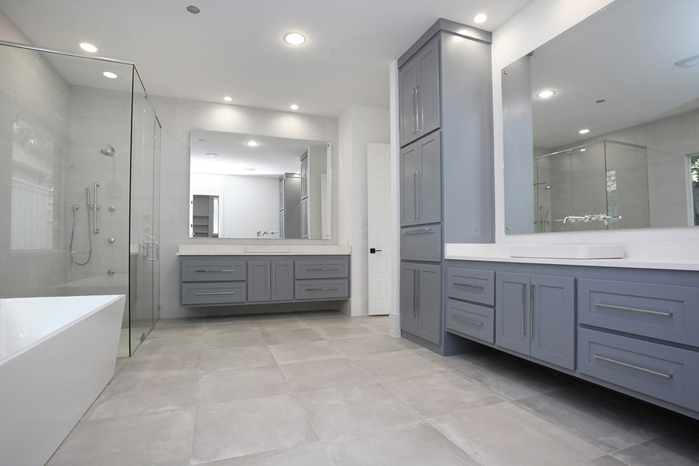 Photo of a large transitional master bathroom in Dallas with shaker cabinets, grey cabinets, a freestanding tub, a corner shower, a one-piece toilet, gray tile, ceramic tile, white walls, ceramic floors, a vessel sink, engineered quartz benchtops, grey floor, a hinged shower door and white benchtops.