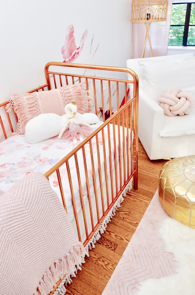 Design ideas for a large transitional nursery for girls with white walls, medium hardwood floors and brown floor.