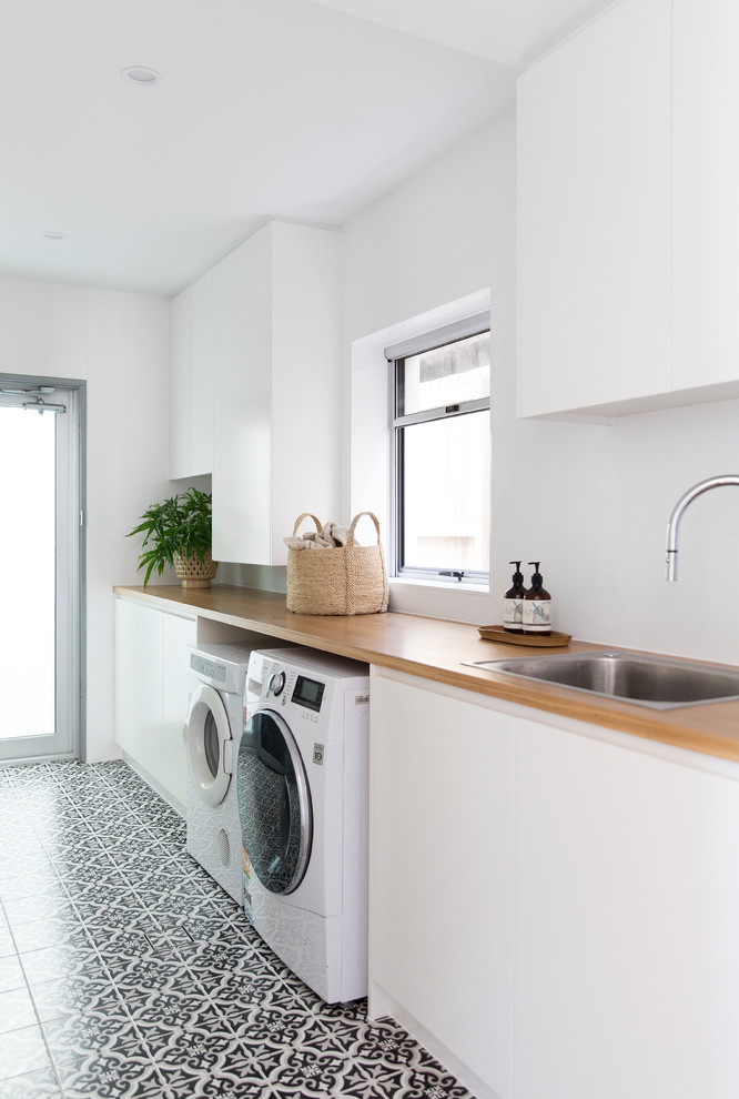 Photo of a mid-sized contemporary single-wall dedicated laundry room in Gold Coast - Tweed with a drop-in sink, flat-panel cabinets, white cabinets, wood benchtops, white walls, a side-by-side washer and dryer, multi-coloured floor and beige benchtop.