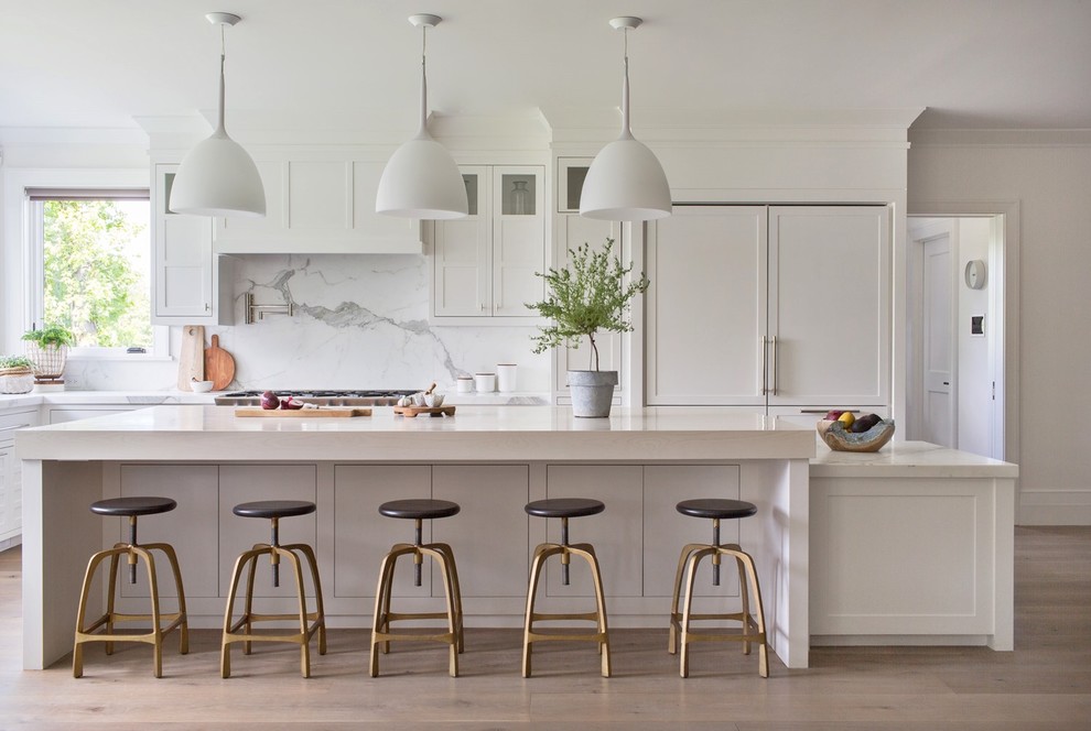 This is an example of an expansive transitional kitchen in Other with white cabinets, shaker cabinets, white splashback, light hardwood floors, with island, beige floor and white benchtop.