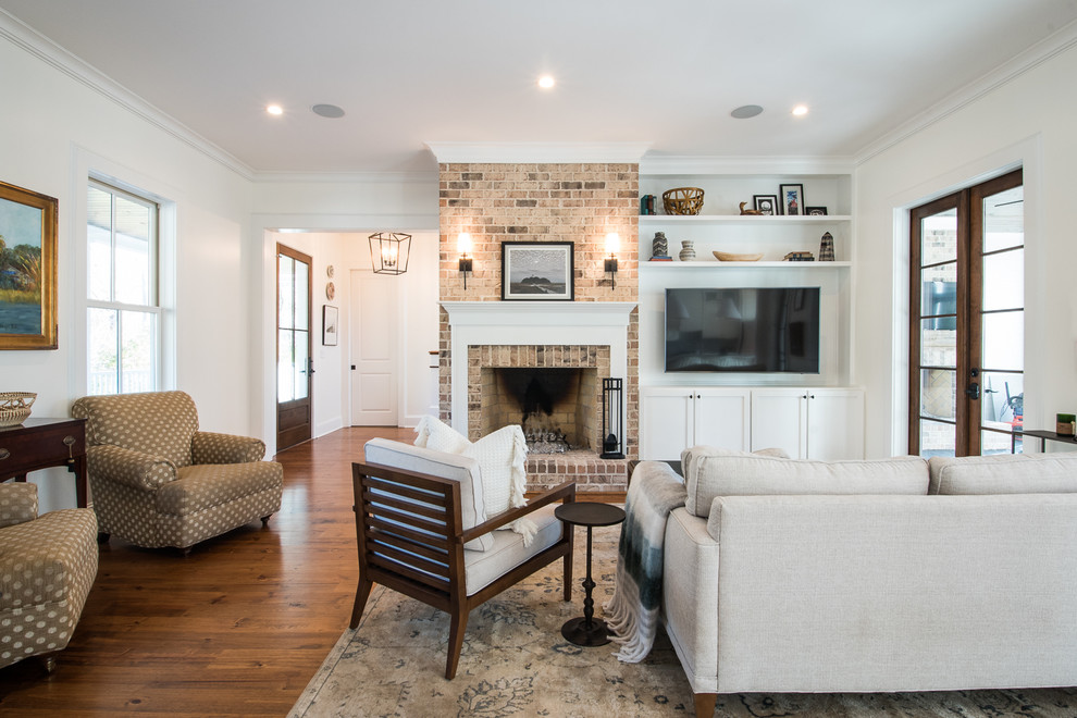 Inspiration for a large transitional open concept living room in Charleston with white walls, medium hardwood floors, a standard fireplace, a brick fireplace surround, a wall-mounted tv and brown floor.