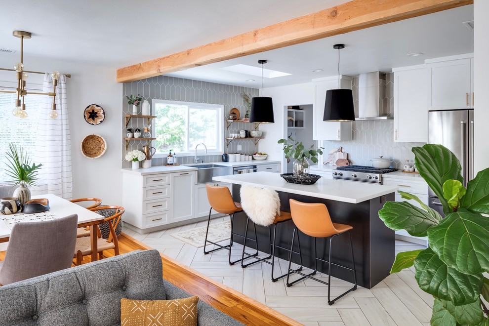 This is an example of a mid-sized transitional l-shaped eat-in kitchen in San Diego with a farmhouse sink, shaker cabinets, black cabinets, quartz benchtops, grey splashback, ceramic splashback, stainless steel appliances, porcelain floors, with island and white benchtop.