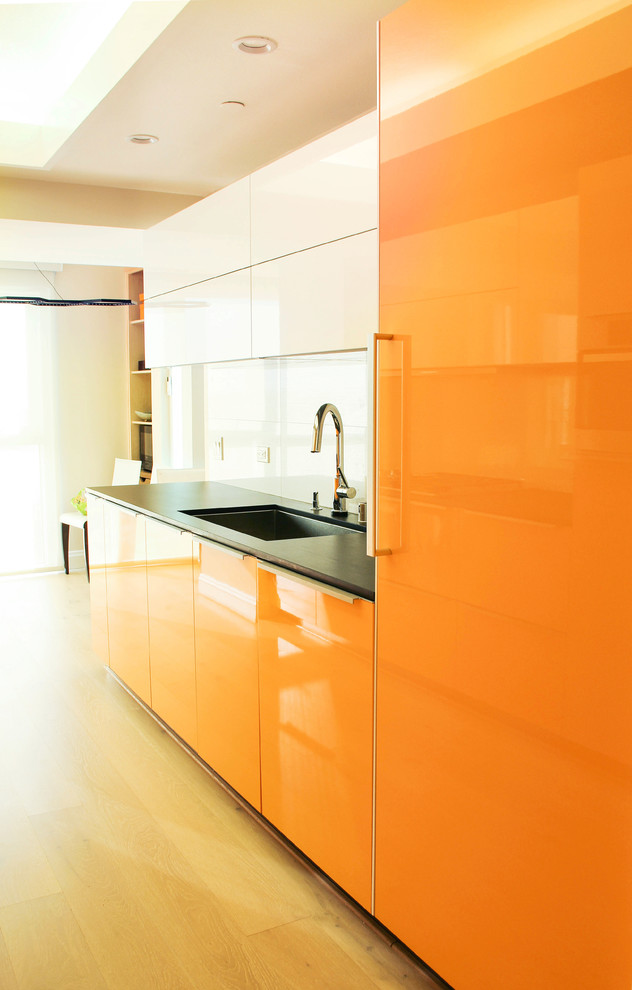 This is an example of a small modern single-wall eat-in kitchen in Los Angeles with a drop-in sink, flat-panel cabinets, orange cabinets, quartz benchtops, black splashback, porcelain splashback, stainless steel appliances, light hardwood floors and no island.