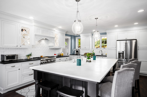 Bright white kitchen with shaker kitchen cabinet runs, subway tile backsplash, oversized island with seating, globe pendants, and stainless-steel appliances.