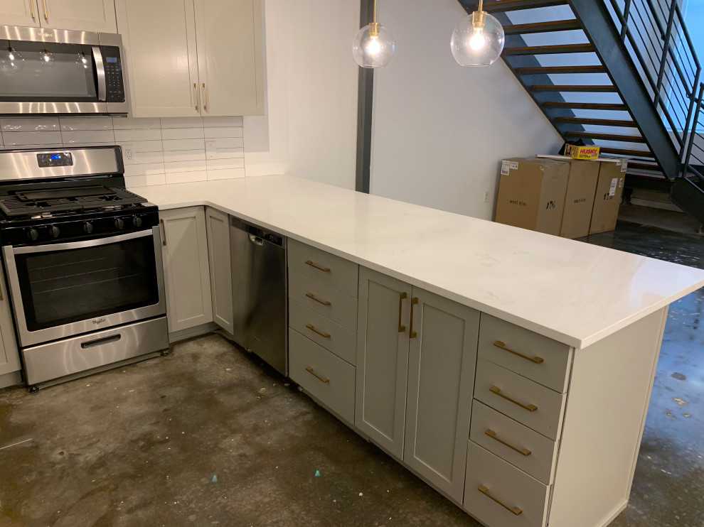 Inspiration for a small industrial u-shaped eat-in kitchen in Atlanta with an undermount sink, shaker cabinets, grey cabinets, quartz benchtops, white splashback, ceramic splashback, stainless steel appliances, concrete floors, a peninsula, grey floor and white benchtop.