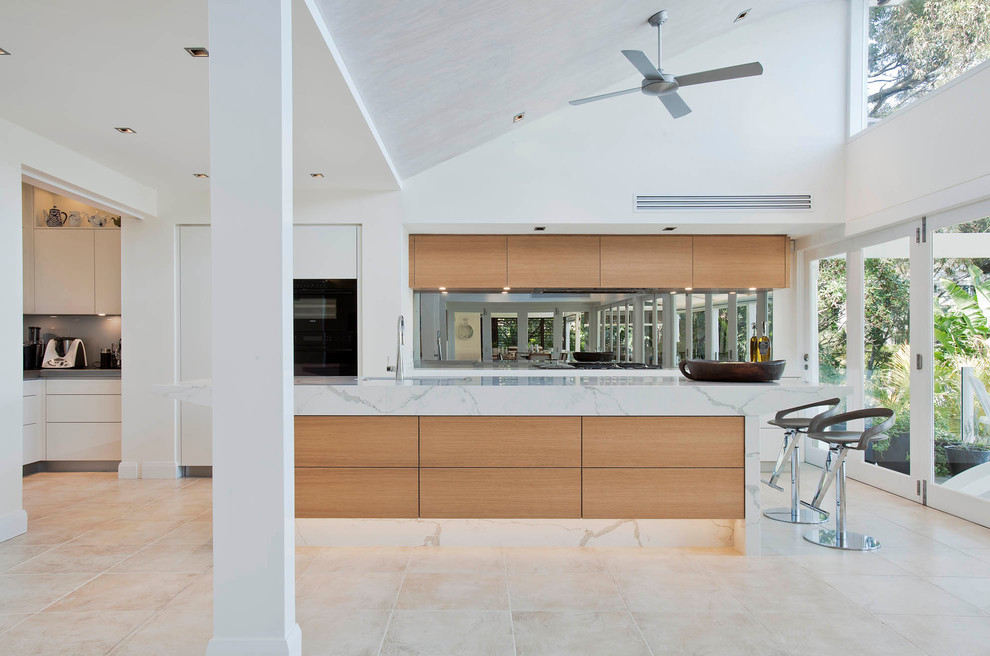 Design ideas for a large modern l-shaped open plan kitchen in Sydney with an undermount sink, flat-panel cabinets, white cabinets, quartz benchtops, grey splashback, mirror splashback, black appliances, limestone floors and with island.