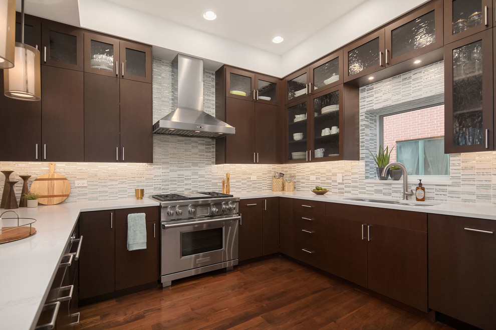 This is an example of a large contemporary u-shaped kitchen in Chicago with a double-bowl sink, flat-panel cabinets, dark wood cabinets, glass tile splashback, dark hardwood floors, brown floor, white splashback, stainless steel appliances, white benchtop, quartzite benchtops and no island.