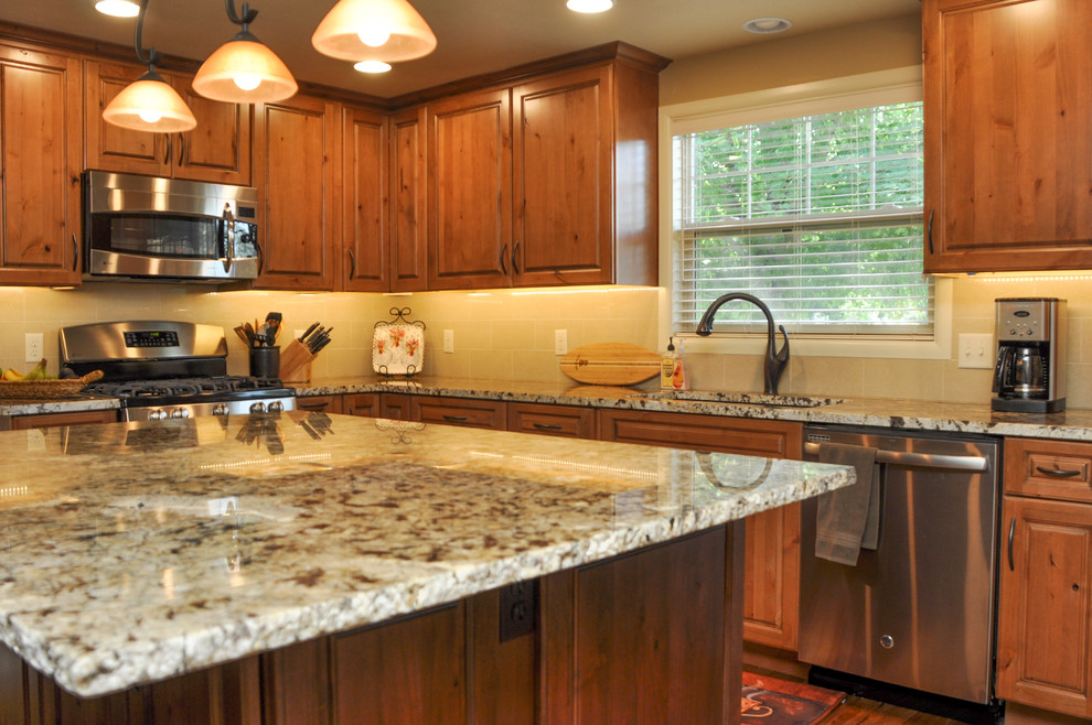Example of a small transitional u-shaped medium tone wood floor kitchen design in Boise with an undermount sink, raised-panel cabinets, medium tone wood cabinets, granite countertops, beige backsplash, porcelain backsplash, stainless steel appliances and an island