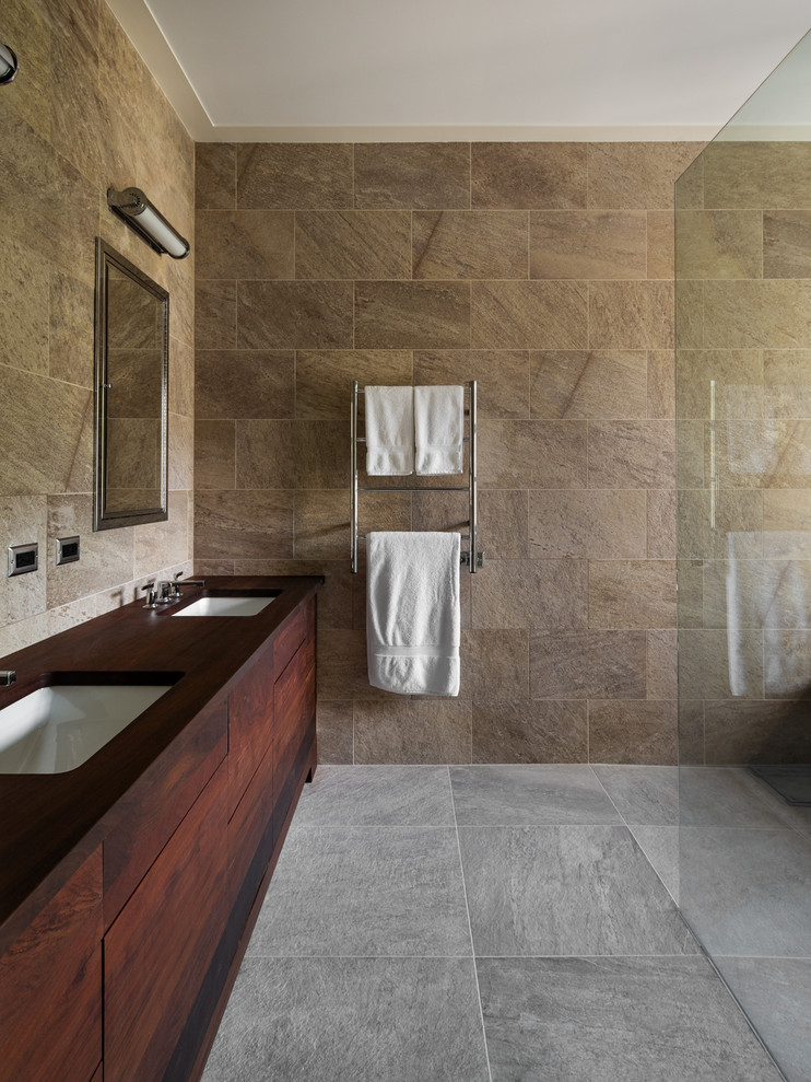 Design ideas for a large country master bathroom in Birmingham with flat-panel cabinets, brown cabinets, an alcove tub, a shower/bathtub combo, a two-piece toilet, brown tile, brown walls, ceramic floors, an undermount sink, wood benchtops, beige floor, an open shower and brown benchtops.