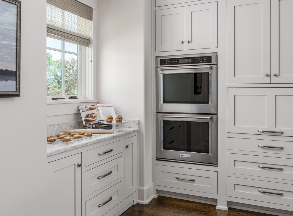 Open concept kitchen - transitional l-shaped dark wood floor and brown floor open concept kitchen idea in Nashville with an undermount sink, white cabinets, quartz countertops, white backsplash, stone tile backsplash, stainless steel appliances, an island, white countertops and shaker cabinets