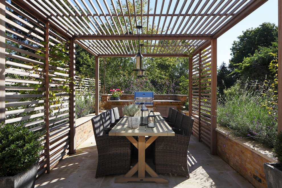 This is an example of a traditional backyard patio in London with an outdoor kitchen, concrete pavers and a pergola.