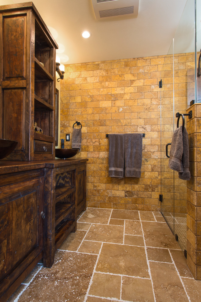 Inspiration for a mid-sized master bathroom in Los Angeles with furniture-like cabinets, distressed cabinets, a curbless shower, a two-piece toilet, yellow tile, travertine, beige walls, travertine floors, a vessel sink, wood benchtops, beige floor and a hinged shower door.