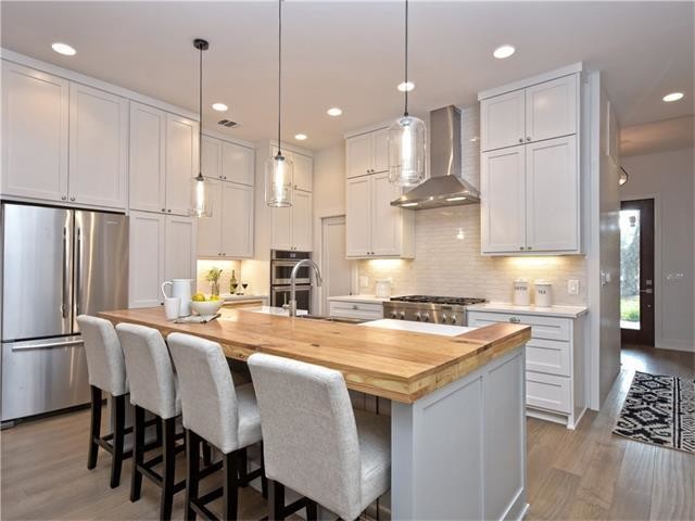 Open concept kitchen - small transitional galley light wood floor and gray floor open concept kitchen idea in Austin with a farmhouse sink, shaker cabinets, white cabinets, wood countertops, white backsplash, ceramic backsplash, stainless steel appliances and an island
