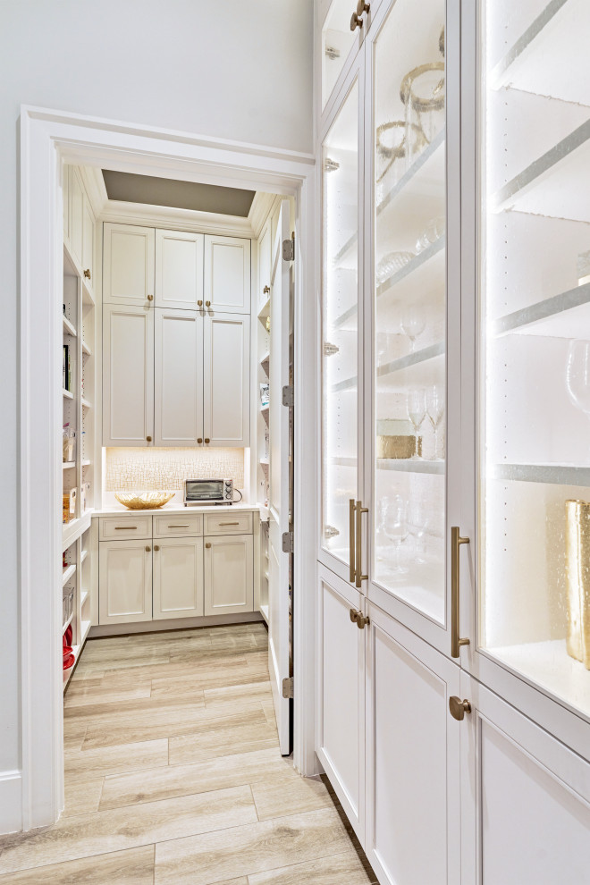 This is an example of a classic kitchen pantry with a built-in sink, stainless steel appliances, beige floors, white worktops, white cabinets, glass-front cabinets, stone tiled splashback and porcelain flooring.