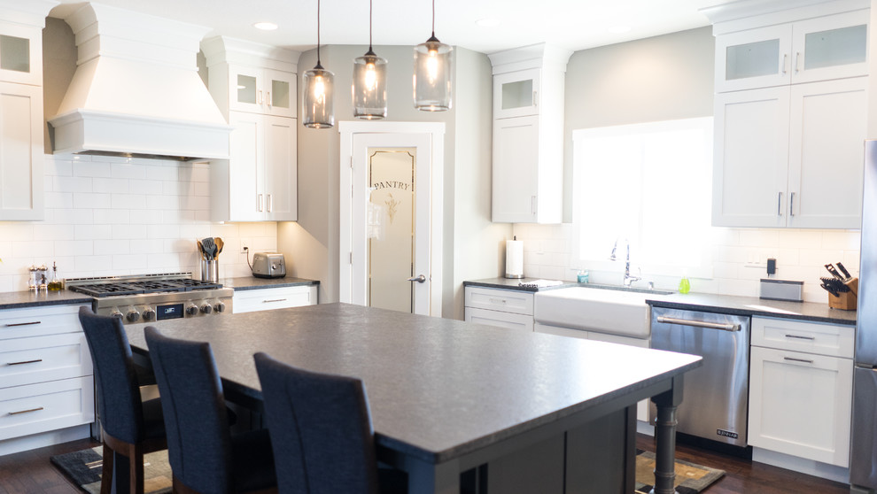 Example of a large transitional u-shaped eat-in kitchen design with a farmhouse sink, flat-panel cabinets, white cabinets, granite countertops, white backsplash, ceramic backsplash, stainless steel appliances and an island