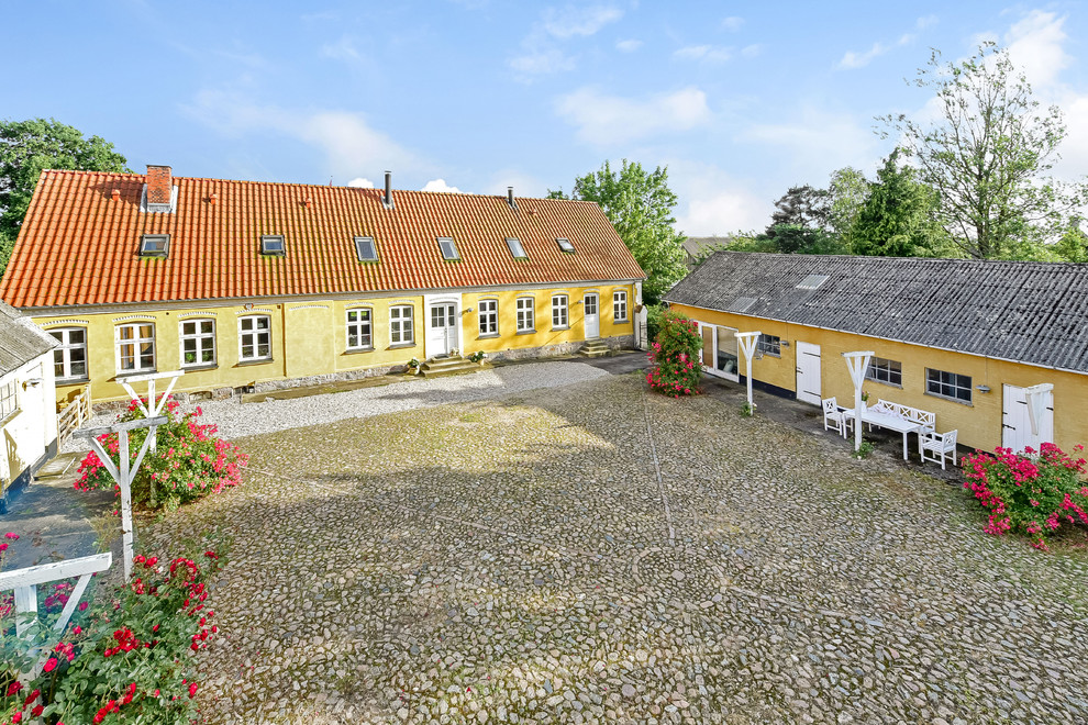 Photo of a large country two-storey yellow house exterior in Copenhagen with a gable roof and a tile roof.