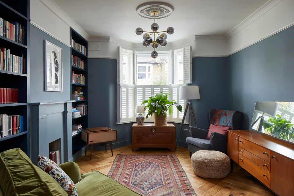 This is an example of a small transitional enclosed living room in London with a library, blue walls, medium hardwood floors, a standard fireplace, a plaster fireplace surround and brown floor.