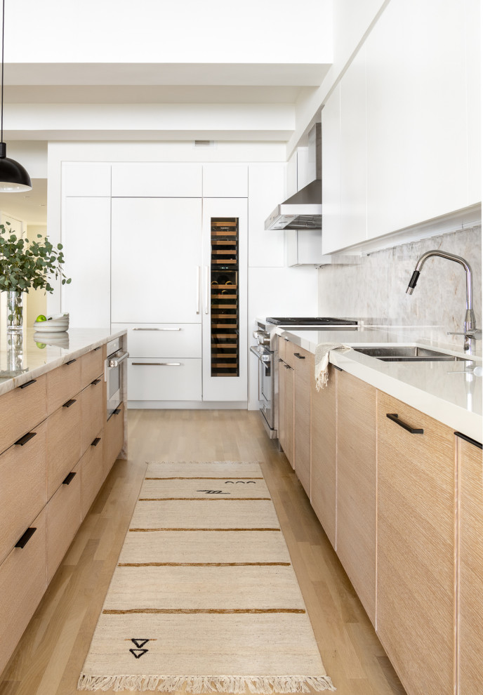 Inspiration for a large contemporary single-wall eat-in kitchen in New York with an undermount sink, flat-panel cabinets, white cabinets, quartzite benchtops, grey splashback, stone slab splashback, stainless steel appliances, light hardwood floors, with island and white benchtop.