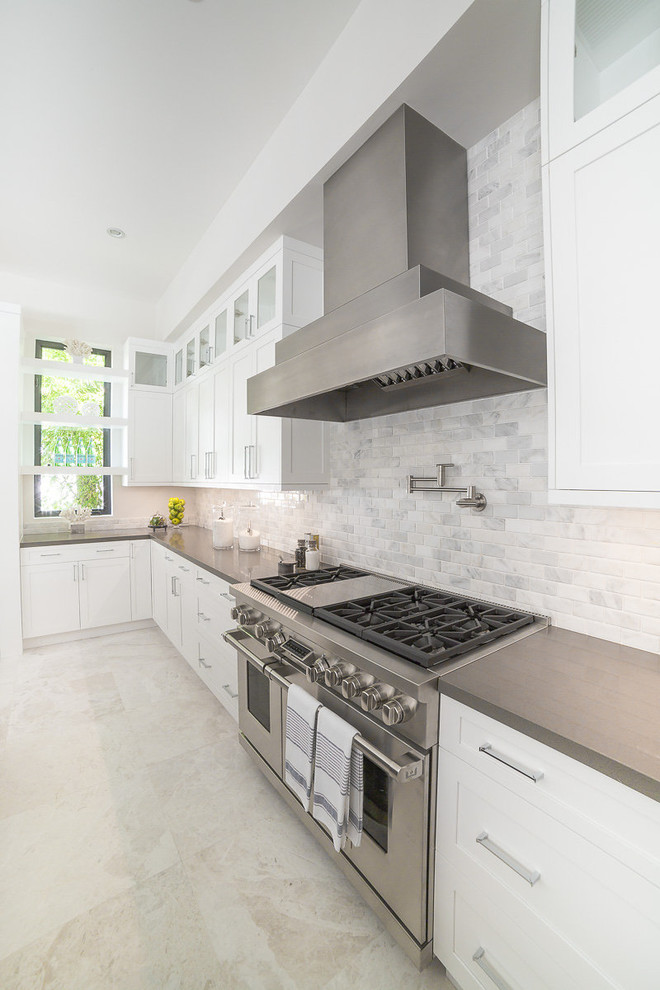 Photo of an expansive contemporary l-shaped open plan kitchen in Miami with an undermount sink, shaker cabinets, white cabinets, quartzite benchtops, beige splashback, stone tile splashback, stainless steel appliances, porcelain floors, with island, white floor and black benchtop.