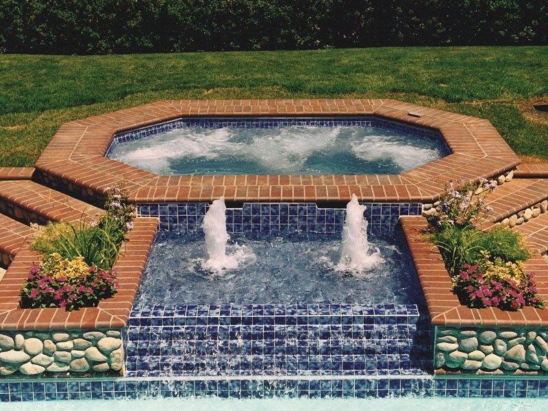 Example of a backyard stone and custom-shaped hot tub design