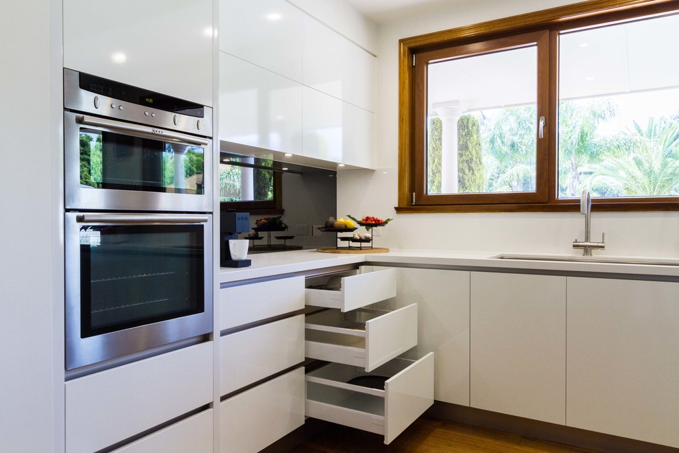 Large contemporary u-shaped eat-in kitchen in Melbourne with an undermount sink, flat-panel cabinets, quartz benchtops, mirror splashback, stainless steel appliances, medium hardwood floors and with island.