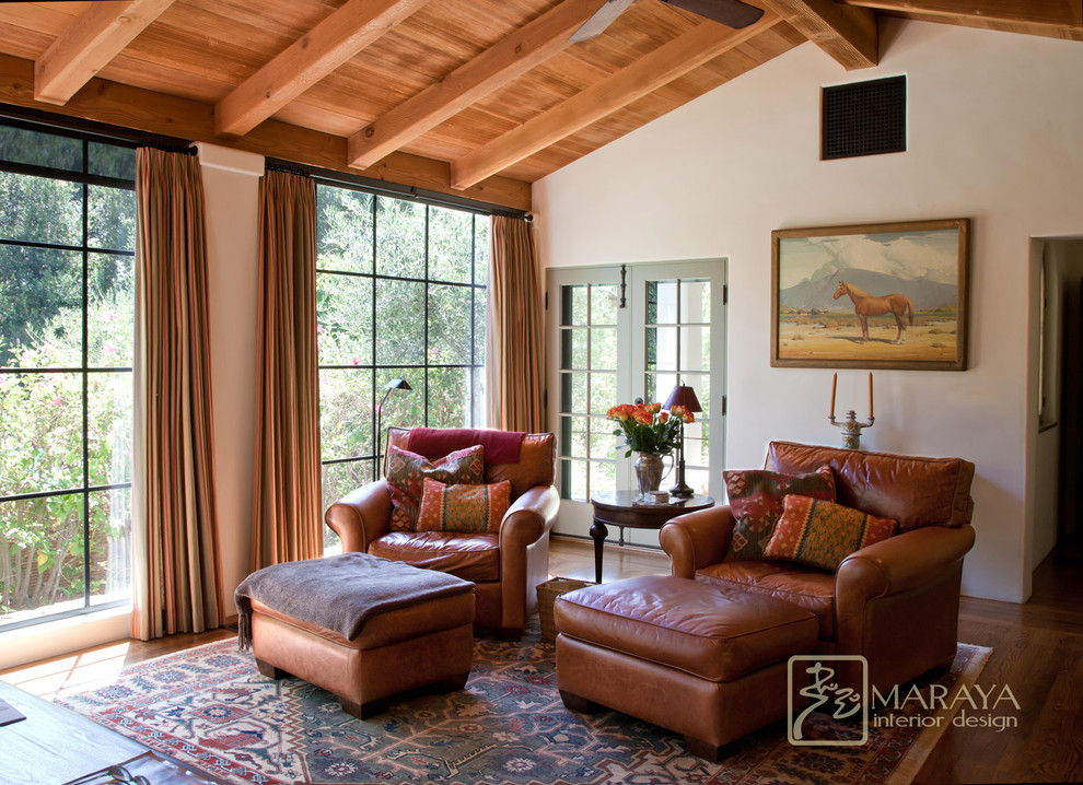Inspiration for a mid-sized mediterranean open concept family room in Santa Barbara with a library, white walls, medium hardwood floors and a wall-mounted tv.
