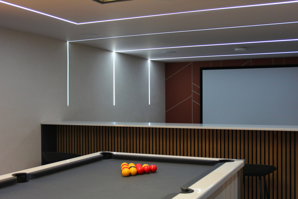 Стильный дизайн: большая открытая комната для игр:: освещение в стиле модернизм с телевизором на стене, синим полом и панелями на части стены - последний тренд
