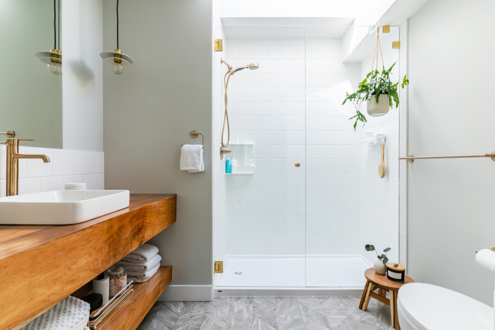Bild på ett funkis brun brunt badrum, med öppna hyllor, skåp i mellenmörkt trä, en dusch i en alkov, vit kakel, gröna väggar, ett fristående handfat, träbänkskiva, grått golv och dusch med gångjärnsdörr