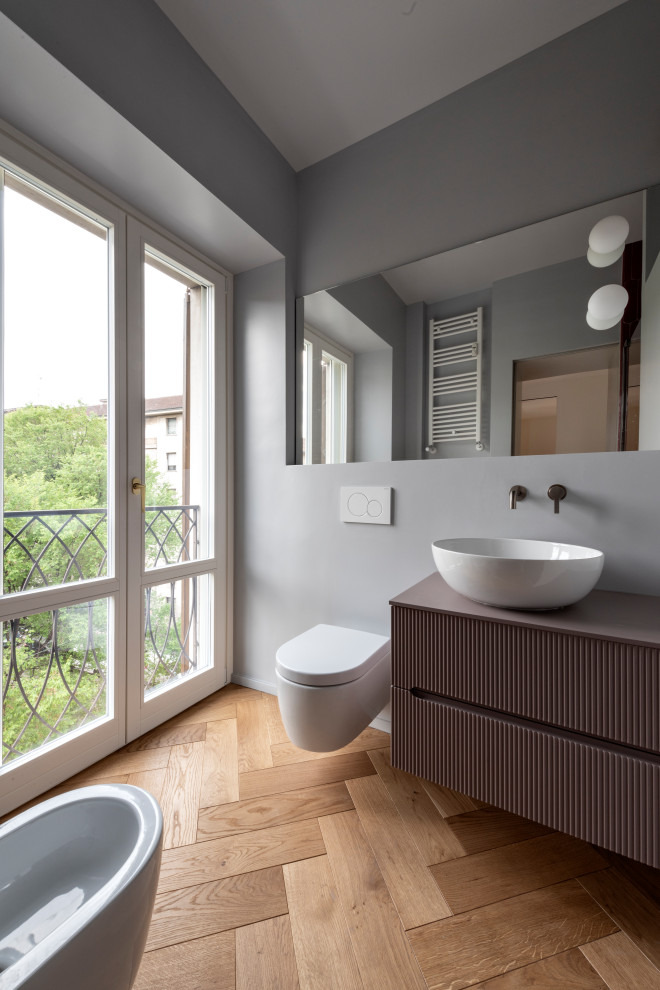 Modern inredning av ett mellanstort lila lila badrum med dusch, med luckor med upphöjd panel, lila skåp, en dusch i en alkov, en vägghängd toalettstol, rosa kakel, porslinskakel, grå väggar, mellanmörkt trägolv, ett fristående handfat, träbänkskiva och dusch med gångjärnsdörr
