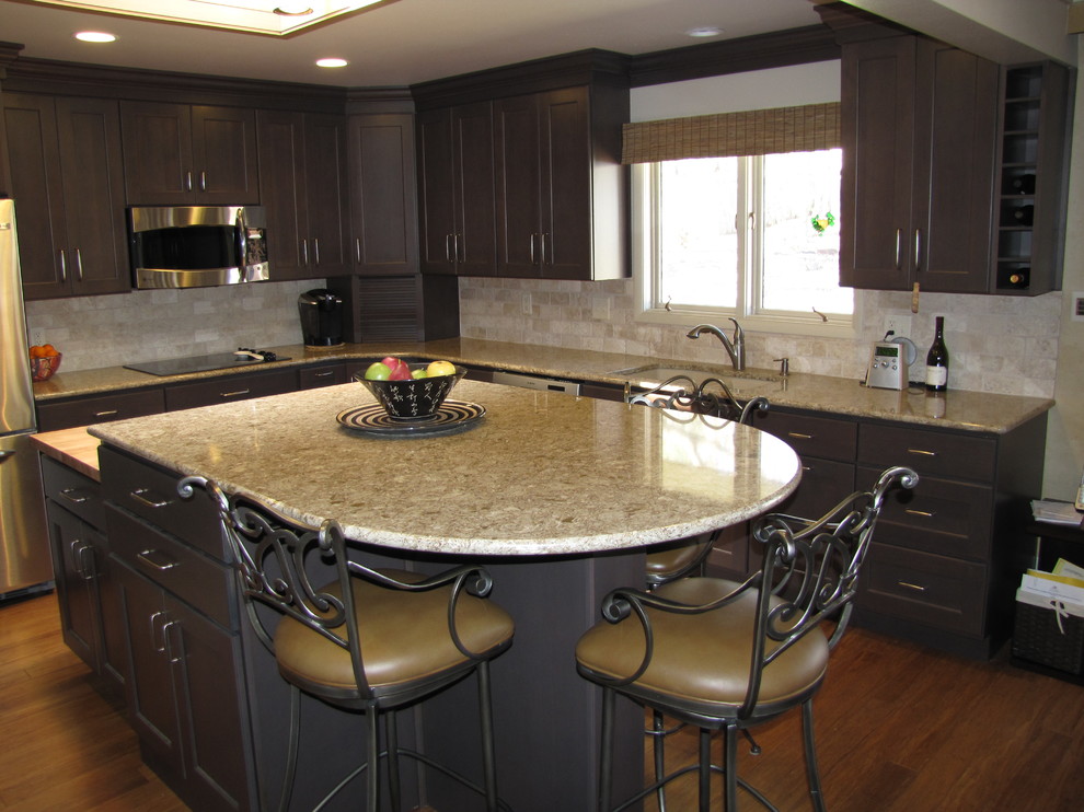 Mid-sized transitional l-shaped bamboo floor enclosed kitchen photo with an undermount sink, recessed-panel cabinets, dark wood cabinets, quartz countertops, beige backsplash, stone tile backsplash, stainless steel appliances and an island