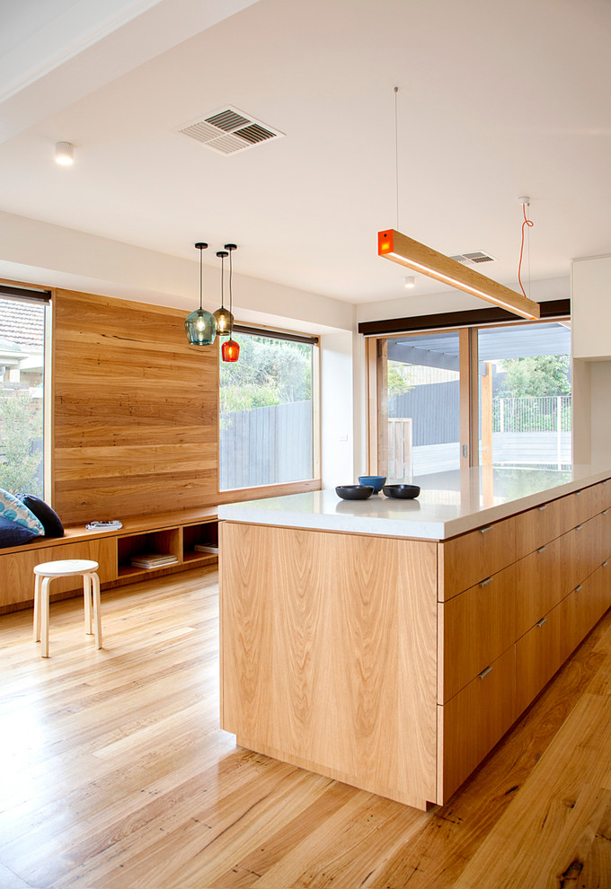 This is an example of a mid-sized contemporary galley eat-in kitchen in Melbourne with an integrated sink, flat-panel cabinets, light wood cabinets, white splashback, subway tile splashback, white appliances, light hardwood floors, with island and solid surface benchtops.