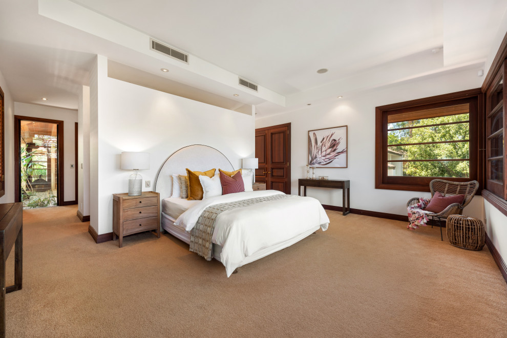 Large contemporary master bedroom in Brisbane with white walls, carpet and brown floor.