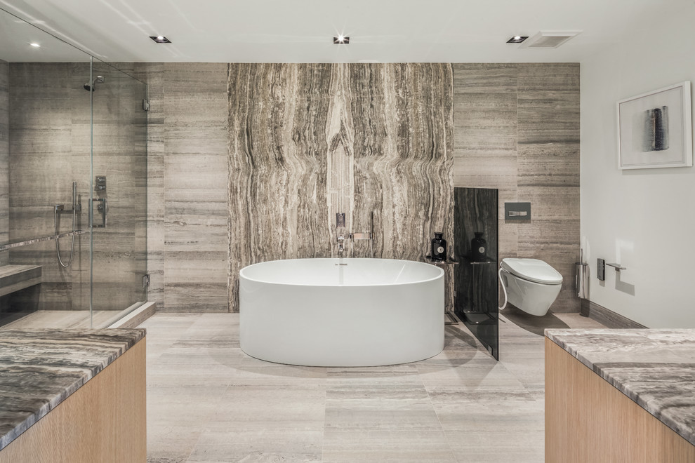 Design ideas for a large contemporary master bathroom in New York with light wood cabinets, a freestanding tub, an alcove shower, a wall-mount toilet, gray tile, grey walls, marble floors, onyx benchtops, grey floor, a hinged shower door and grey benchtops.