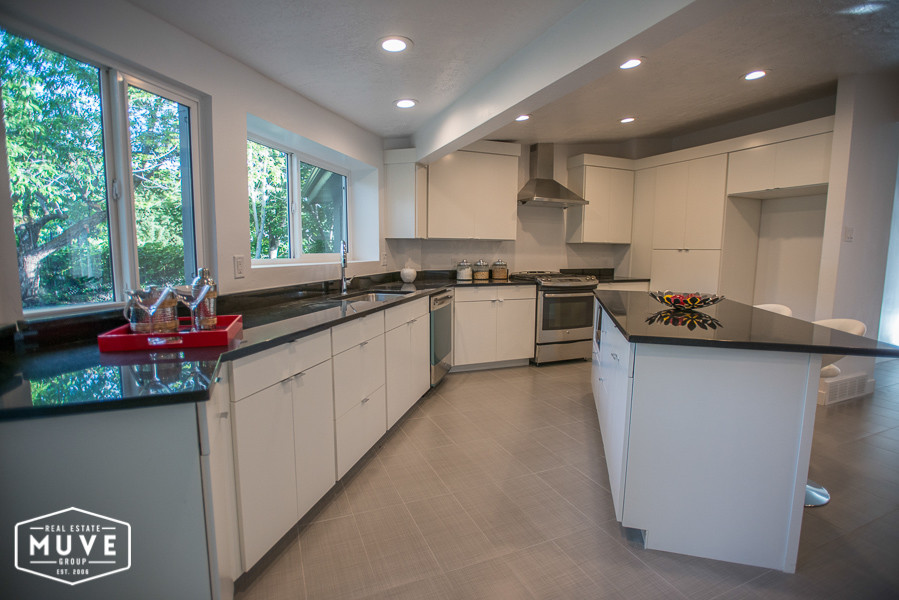 Expansive contemporary l-shaped open plan kitchen in Salt Lake City with an undermount sink, flat-panel cabinets, white cabinets, granite benchtops, black splashback, stainless steel appliances, ceramic floors and a peninsula.