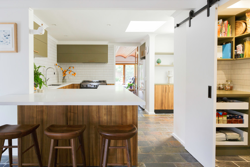 This is an example of a large contemporary u-shaped kitchen in Melbourne with green cabinets, solid surface benchtops, white splashback, stainless steel appliances, limestone floors, white benchtop, an undermount sink, flat-panel cabinets, matchstick tile splashback and a peninsula.
