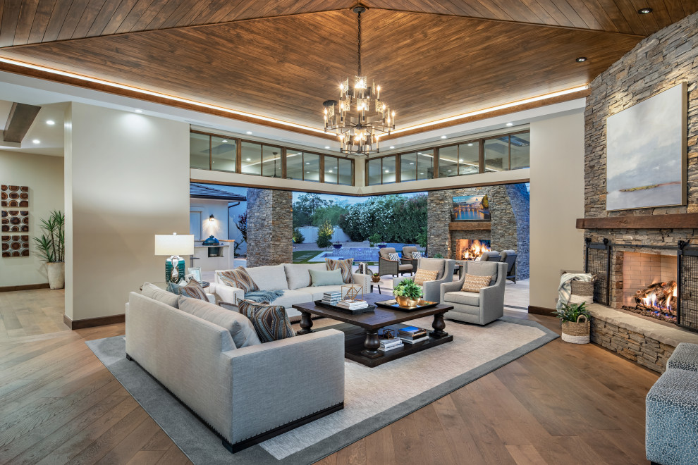 This is an example of a large country formal open concept living room in Phoenix with grey walls, medium hardwood floors, a standard fireplace, a stone fireplace surround, a built-in media wall and brown floor.