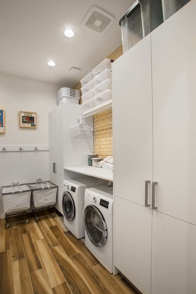 Inspiration for a mid-sized midcentury l-shaped dedicated laundry room in Dallas with flat-panel cabinets, white cabinets, laminate benchtops, white walls, light hardwood floors, a side-by-side washer and dryer, beige floor and white benchtop.