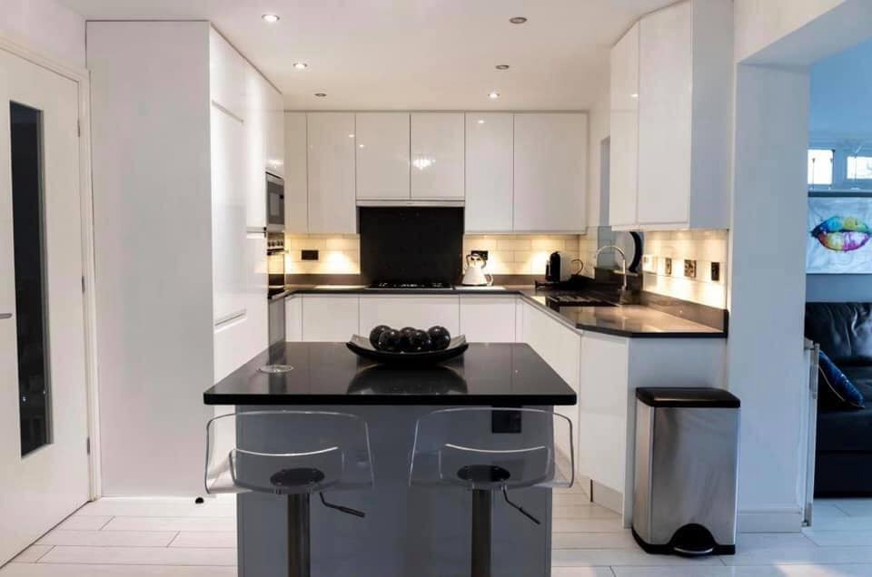 Design ideas for a modern u-shaped kitchen in West Midlands with an undermount sink, white cabinets, black splashback, panelled appliances, with island, black benchtop and granite benchtops.