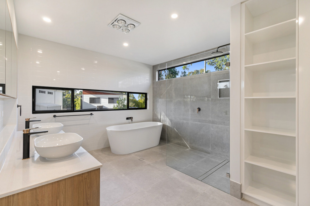 Large modern master bathroom in Brisbane with flat-panel cabinets, brown cabinets, a freestanding tub, a corner shower, gray tile, ceramic tile, grey walls, ceramic floors, a vessel sink, engineered quartz benchtops, grey floor, an open shower, white benchtops, a double vanity and a floating vanity.