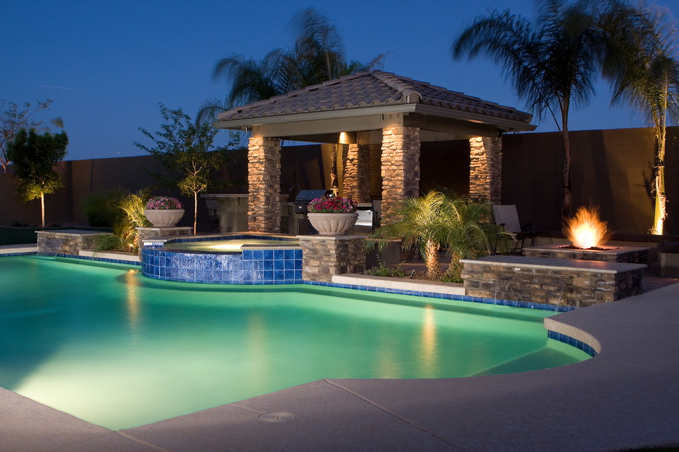 This is an example of a large mediterranean backyard custom-shaped pool in Phoenix with a pool house and natural stone pavers.