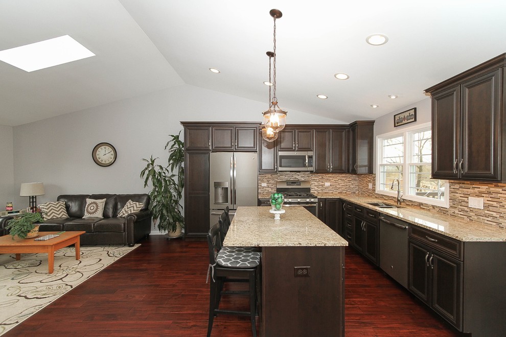 This is an example of a mid-sized transitional l-shaped eat-in kitchen in Chicago with a double-bowl sink, recessed-panel cabinets, dark wood cabinets, granite benchtops, brown splashback, glass tile splashback, stainless steel appliances, medium hardwood floors, with island and brown floor.