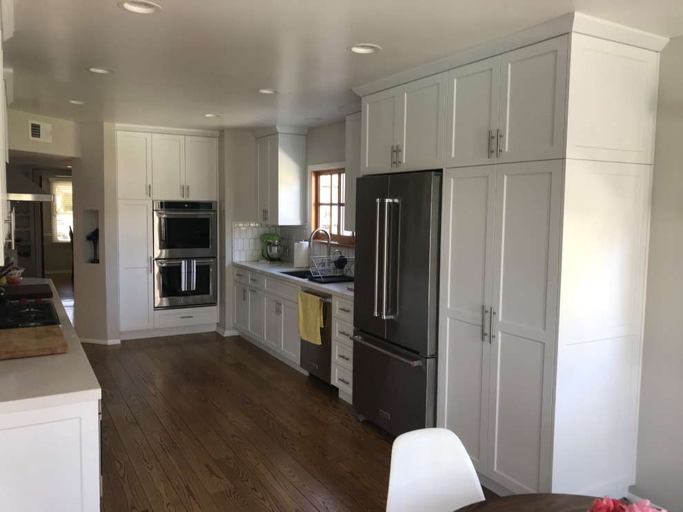Inspiration for a traditional u-shaped eat-in kitchen in Portland with an undermount sink, shaker cabinets, white cabinets, white splashback, subway tile splashback, stainless steel appliances, dark hardwood floors, no island, brown floor, white benchtop and quartz benchtops.