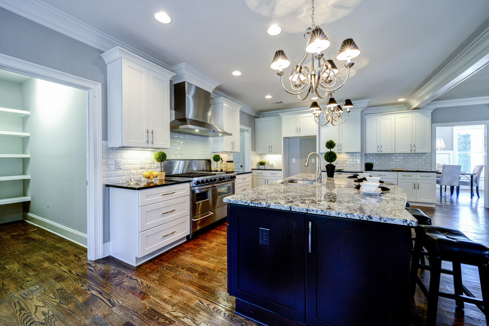 Large traditional l-shaped open plan kitchen in Atlanta with a double-bowl sink, flat-panel cabinets, white cabinets, granite benchtops, white splashback, subway tile splashback, stainless steel appliances, medium hardwood floors and with island.