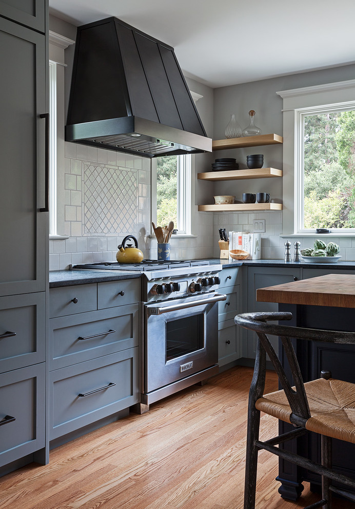 Inspiration for a mid-sized arts and crafts l-shaped separate kitchen in San Francisco with a farmhouse sink, shaker cabinets, grey cabinets, soapstone benchtops, white splashback, ceramic splashback, stainless steel appliances, light hardwood floors, with island and beige floor.